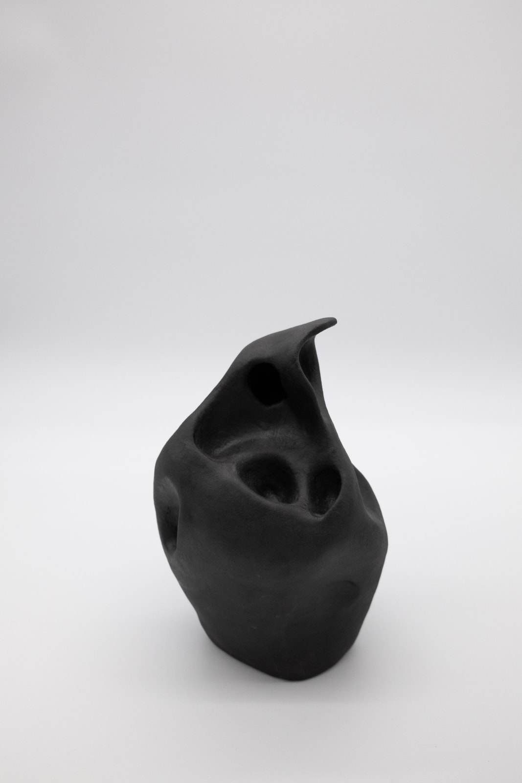 An abstract ceramic sculpture by Emily DiPalo in the shape of a black ghost. The top is pointed and there are random holes throughout.
