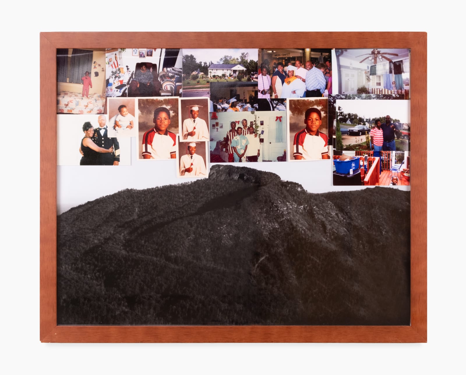 A black and white framed photograph by Mark Anthony Brown Jr of a wooded mountain landscape. Overlaid on top of the glass are several pictures featuring children and families.