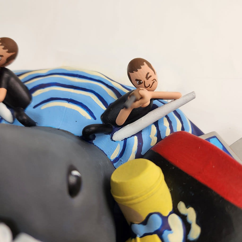 sculpture of a multiple shark heads, humans, and boats coming out towards the viewer