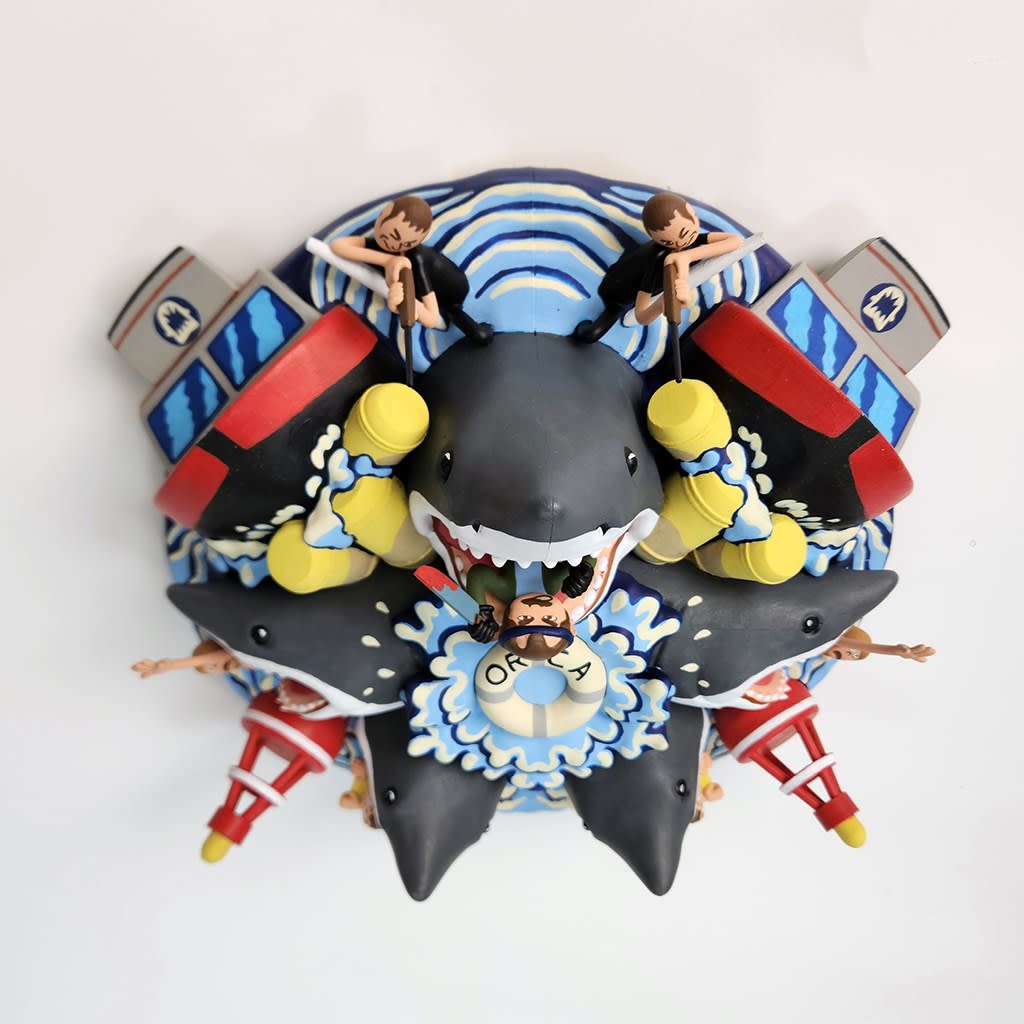 sculpture of a multiple shark heads, humans, and boats coming out towards the viewer
