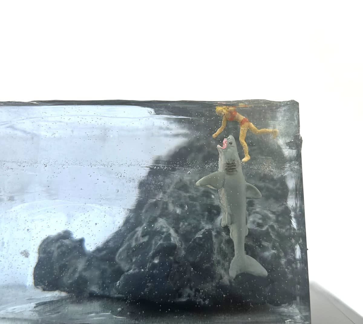 sculpture of a person rowing a boat and another person swimming with a shark coming to eat them