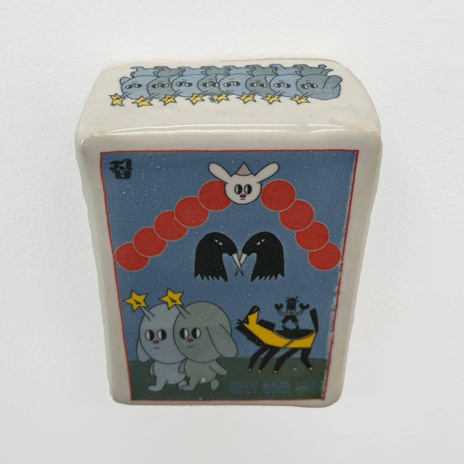 Ceramic sculpture of a card with two crow heads, two dogs with horns with stars, a white rabbit head and a black horse.