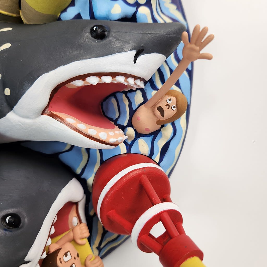 sculpture of a multiple shark heads, humans, and boats coming out towards the viewer