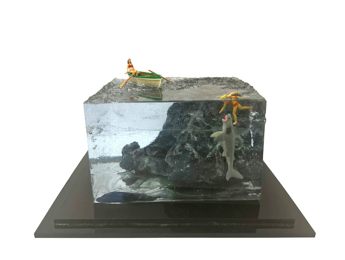 sculpture of a person rowing a boat and another person swimming with a shark coming to eat them