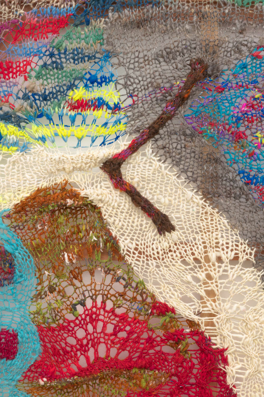 A detail shot of an organic composition with floating geometric accents in multi-colored fibers stretched across a redwood frame as one would stretch a painting. The fibers are knit at varying thicknesses so that in places one can see through the stitches to the wall behind.