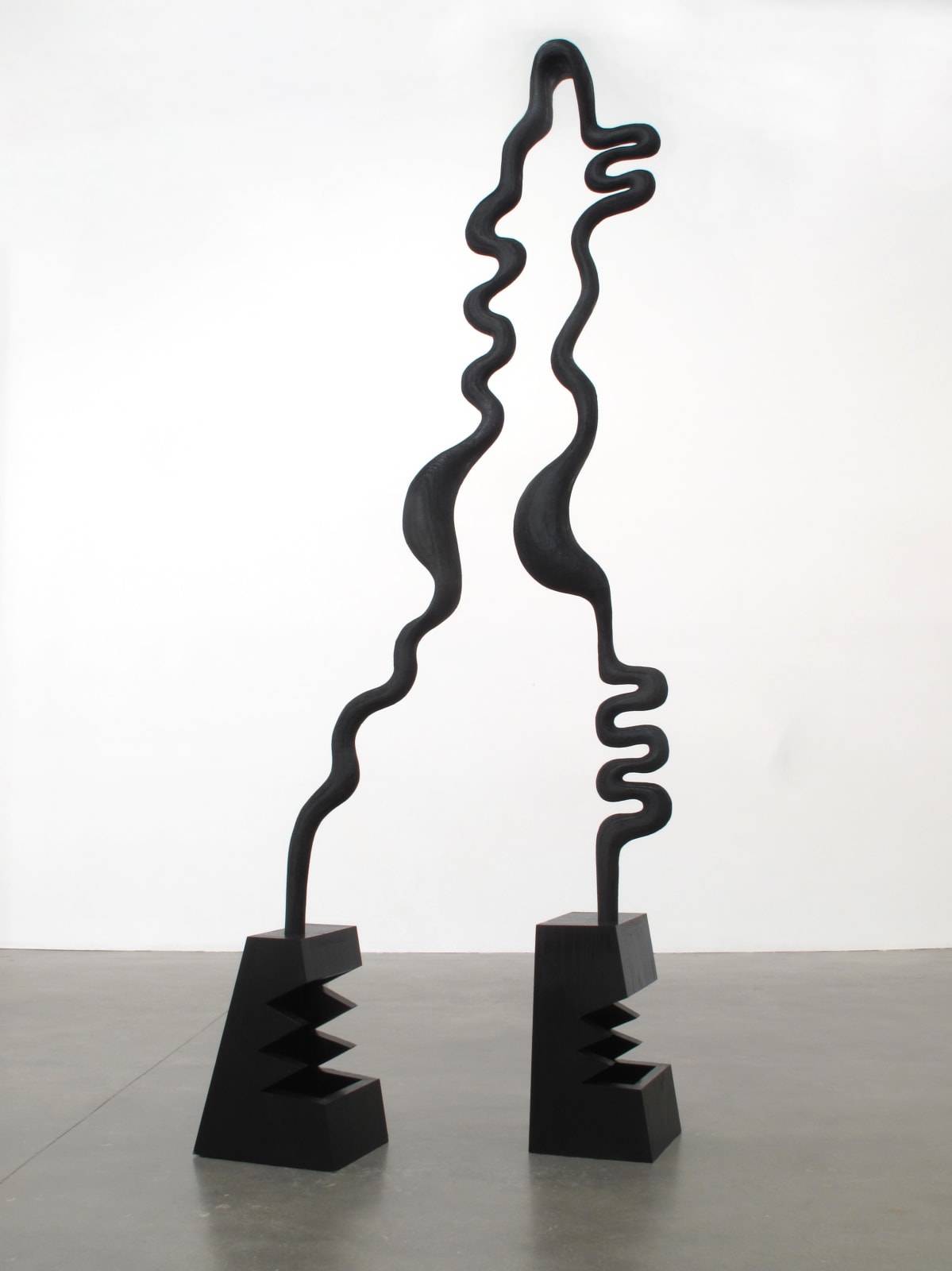 Tall abstract dark wood sculpture with two feet and the profile of head and body