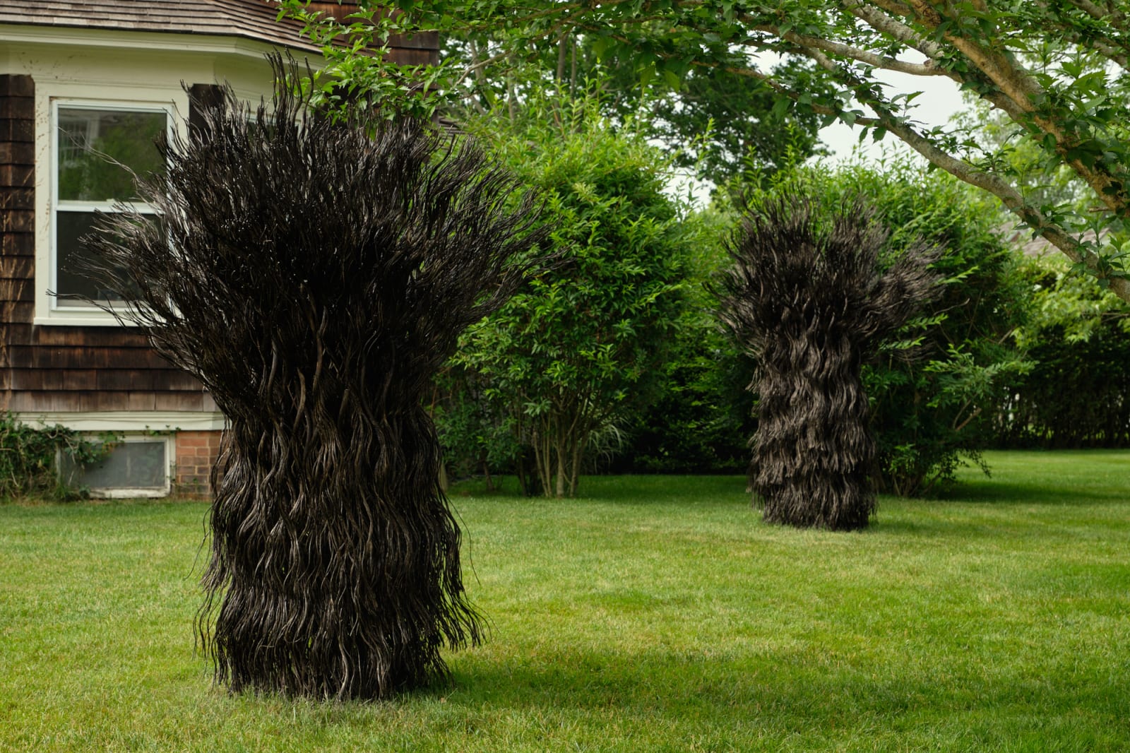 Two large steel sculptures installed at DIA Bridgehampton that resemble gathered wheat shocks placed on a manicured lawn, on the left side of the frame is a window on a cedar-shake building.