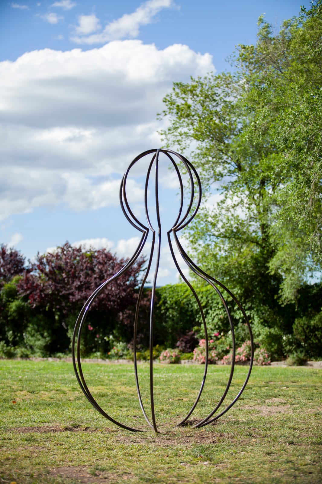Outdoor installation view of a metal sculpture with a small spherical shape on top of a larger spherical body located at Socrates Sculpture Park