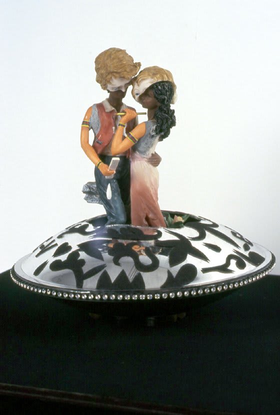 Two ceramic figures made up of several kitsch figurines on a decorated rotating base