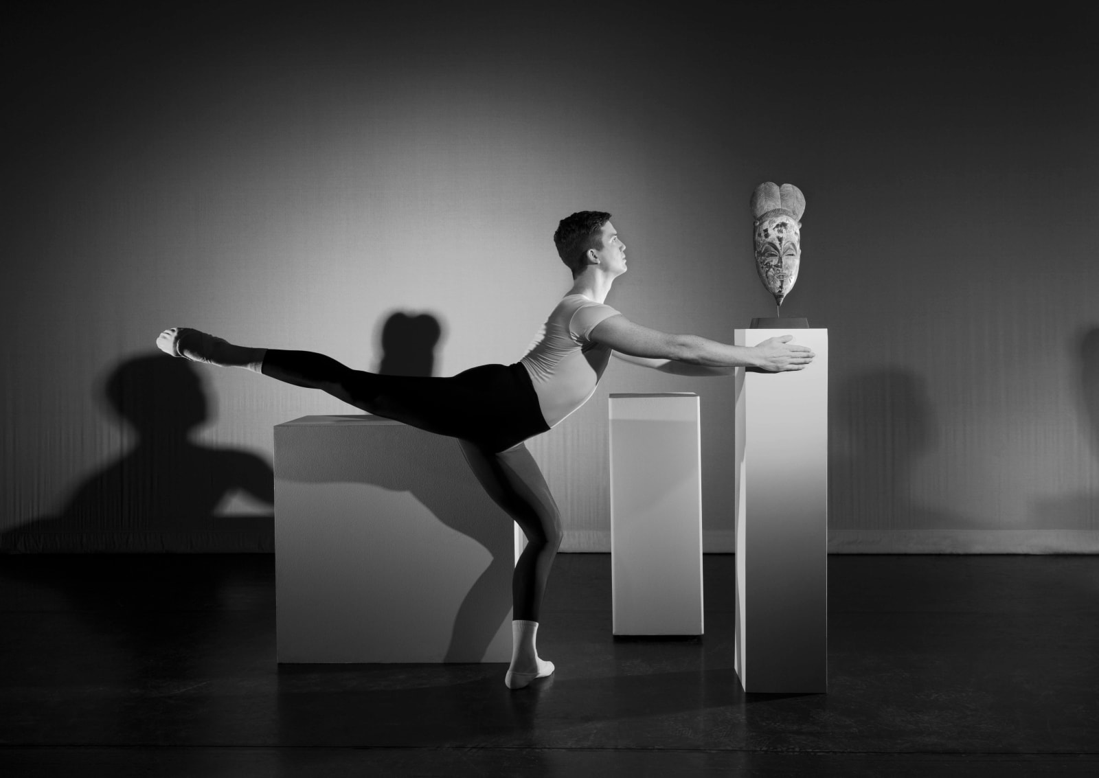 Black and white photograph of mask on pedestal and dancer