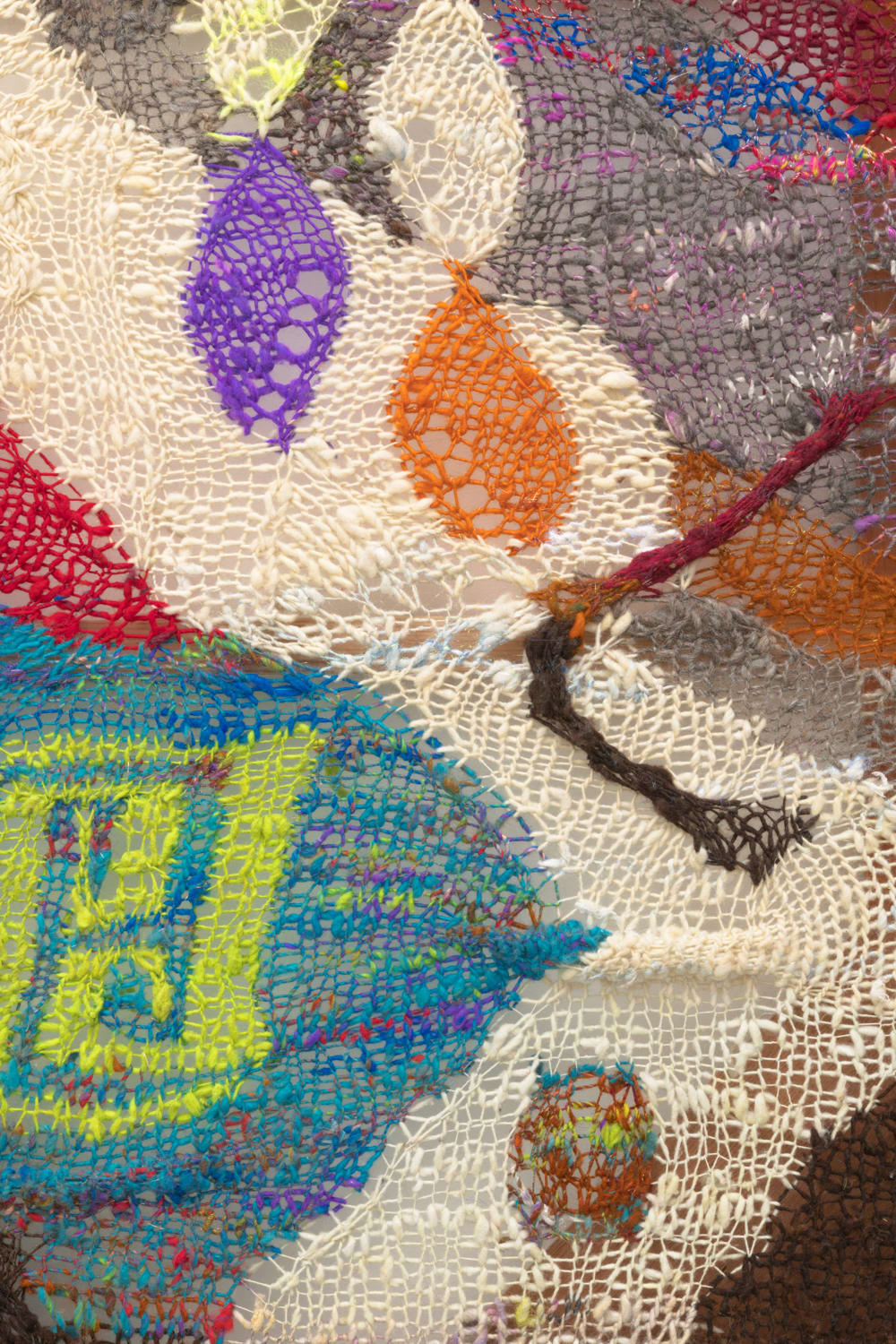 A detail shot of an organic composition with floating geometric accents in multi-colored fibers stretched across a redwood frame as one would stretch a painting. The fibers are knit at varying thicknesses so that in places one can see through the stitches to the wall behind.