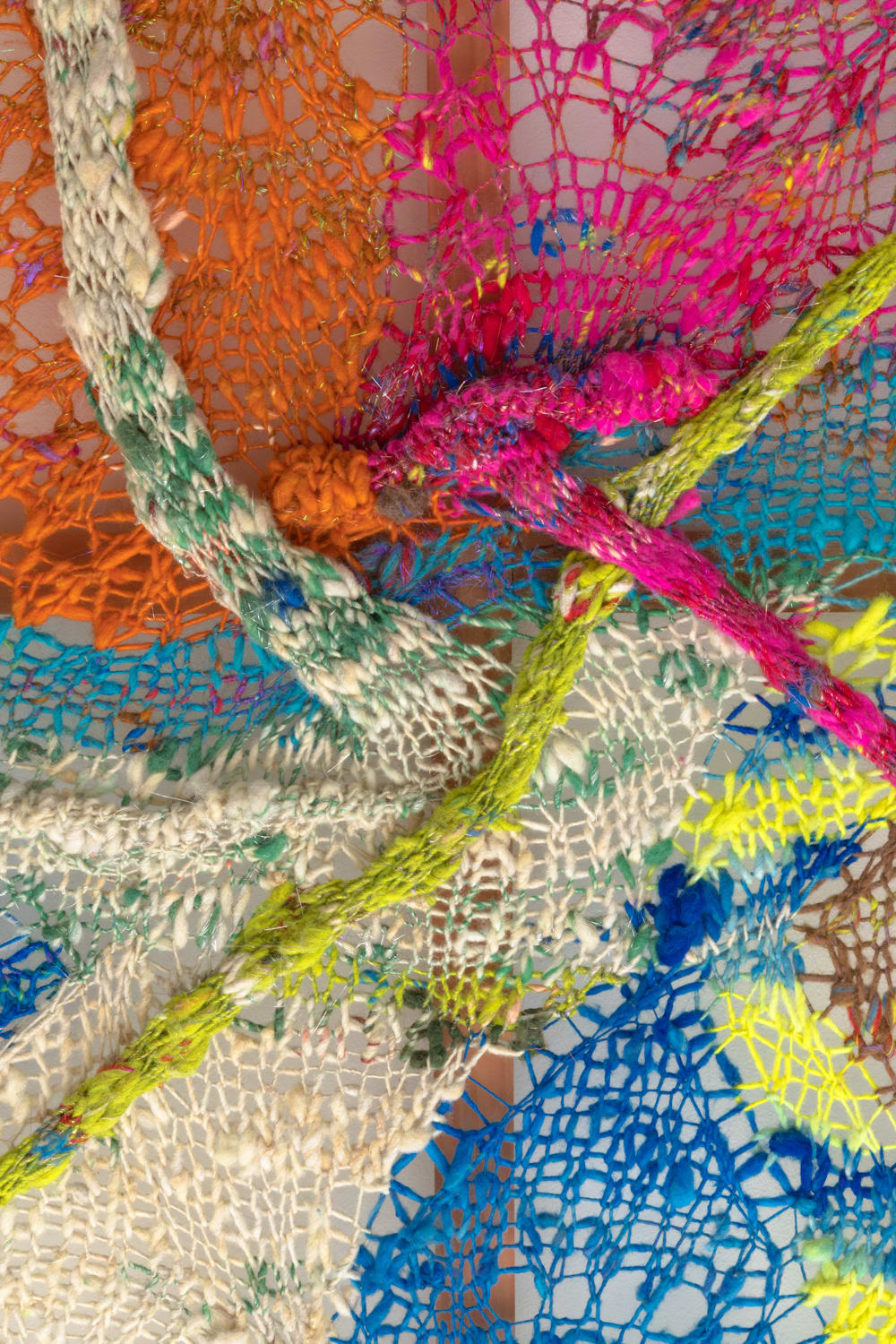A detail of anorganic composition in multi-colored fibers stretched across a redwood frame as one would stretch a painting. The fibers are knit at varying thicknesses so that in places one can see through the stitches to the wall behind.