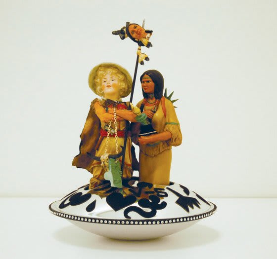 Sculpture made from kitsch ceramics combining Native American figurines with a blonde curly haired boy holding the head of a Native American impaled on a spear