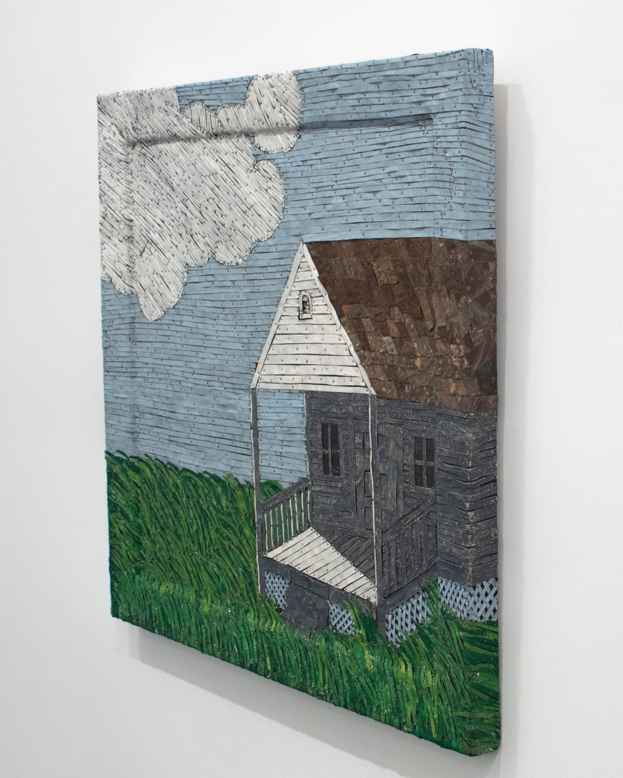 Right angle view of a house sitting under a cloudy sky on a grassy field made from strips of colored tin.