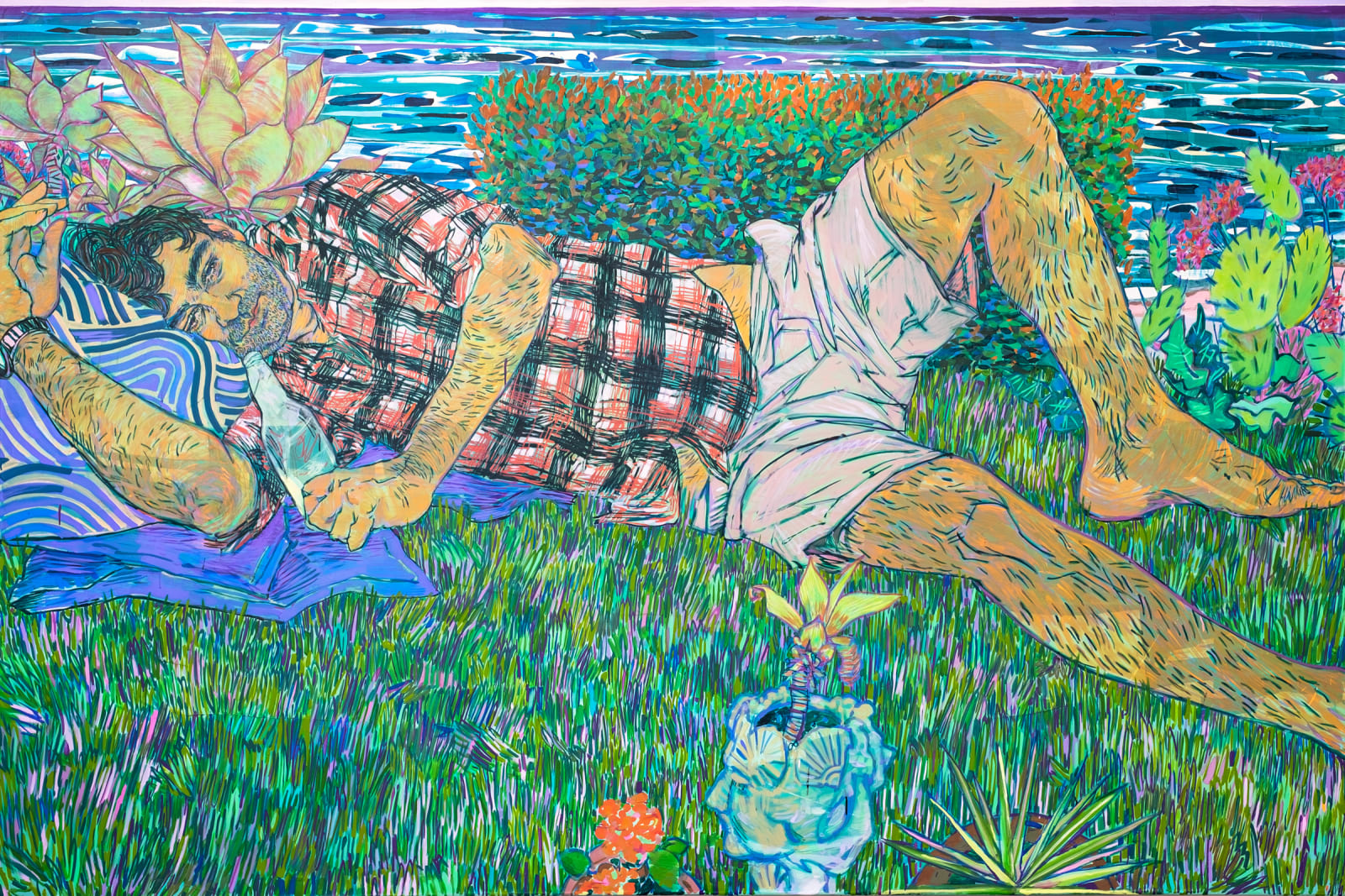 Man in plaid shirt lies down in grass, pillows under his head, water in the background