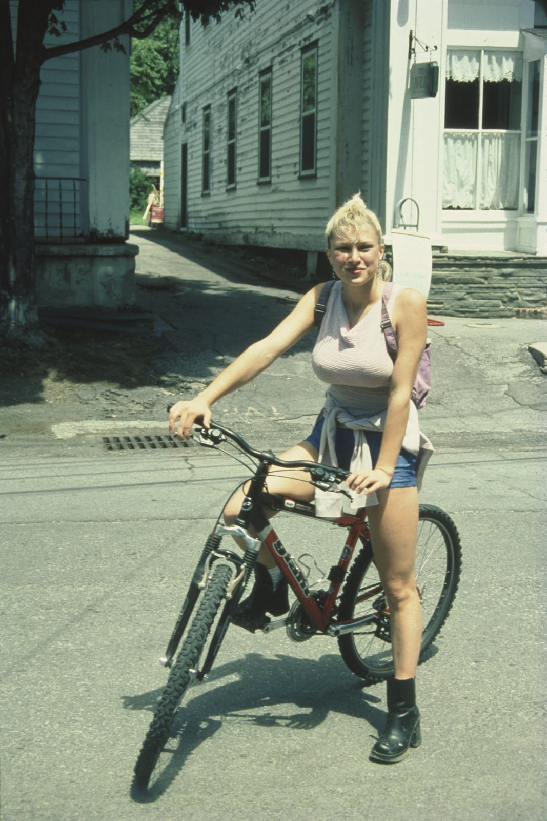 Color photo of a young woman wearing a backpack on a mountain bike, facing the camera and smiling wiith leather ankle-boots