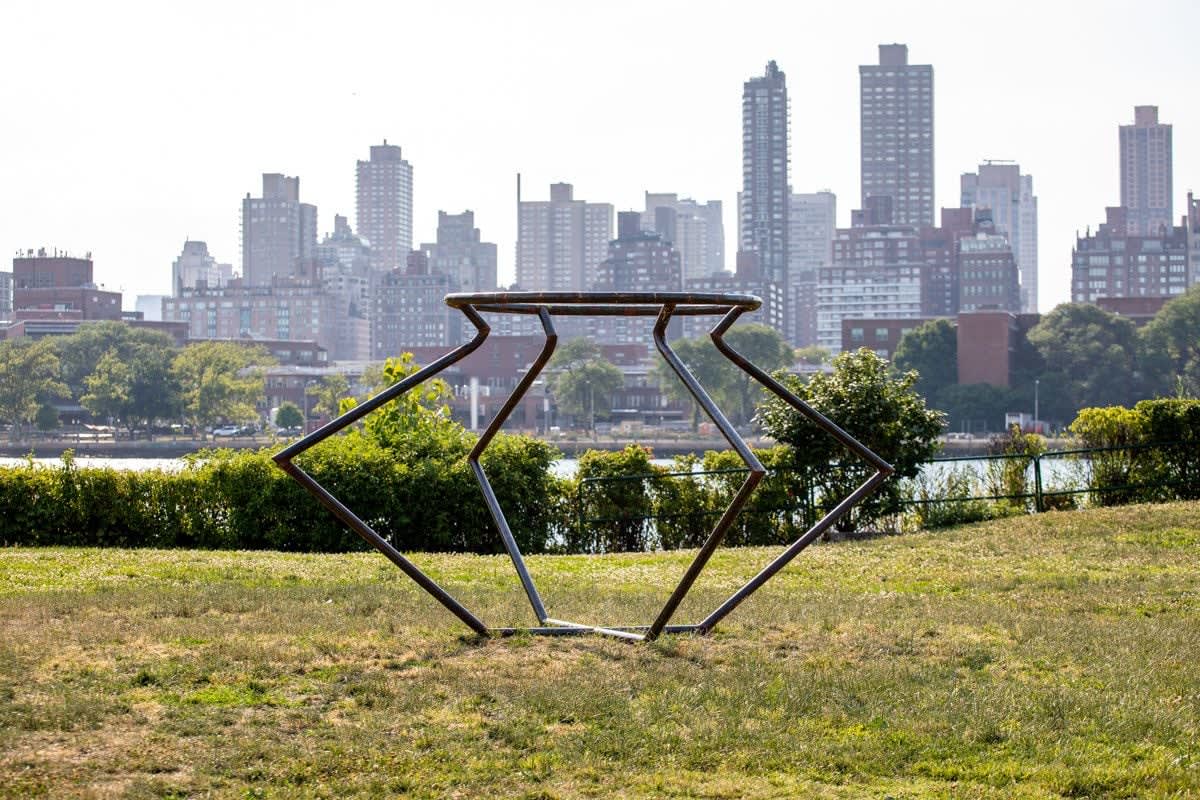 Outdoor installation view of a metal sculpture that resembles an angular vessel set in a green park at Socrates Sculpture Park
