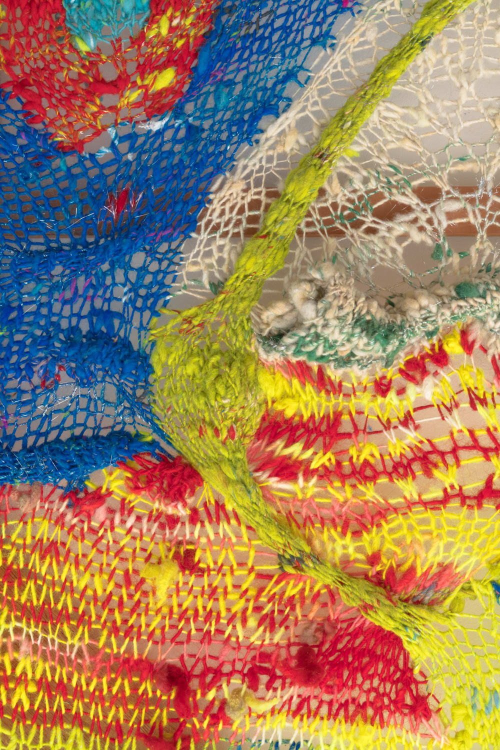 A detail of an organic composition in multi-colored fibers stretched across a redwood frame as one would stretch a painting. The fibers are knit at varying thicknesses so that in places one can see through the stitches to the wall behind.