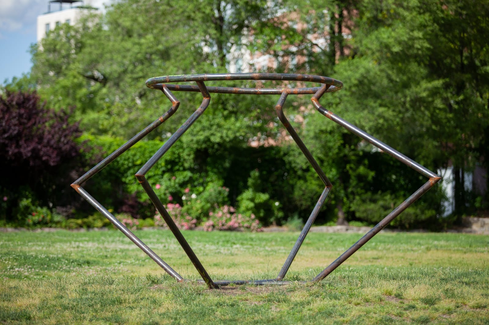 Outdoor installation view of a metal sculpture that resembles an angular vessel set in a green park at Socrates Sculpture Park