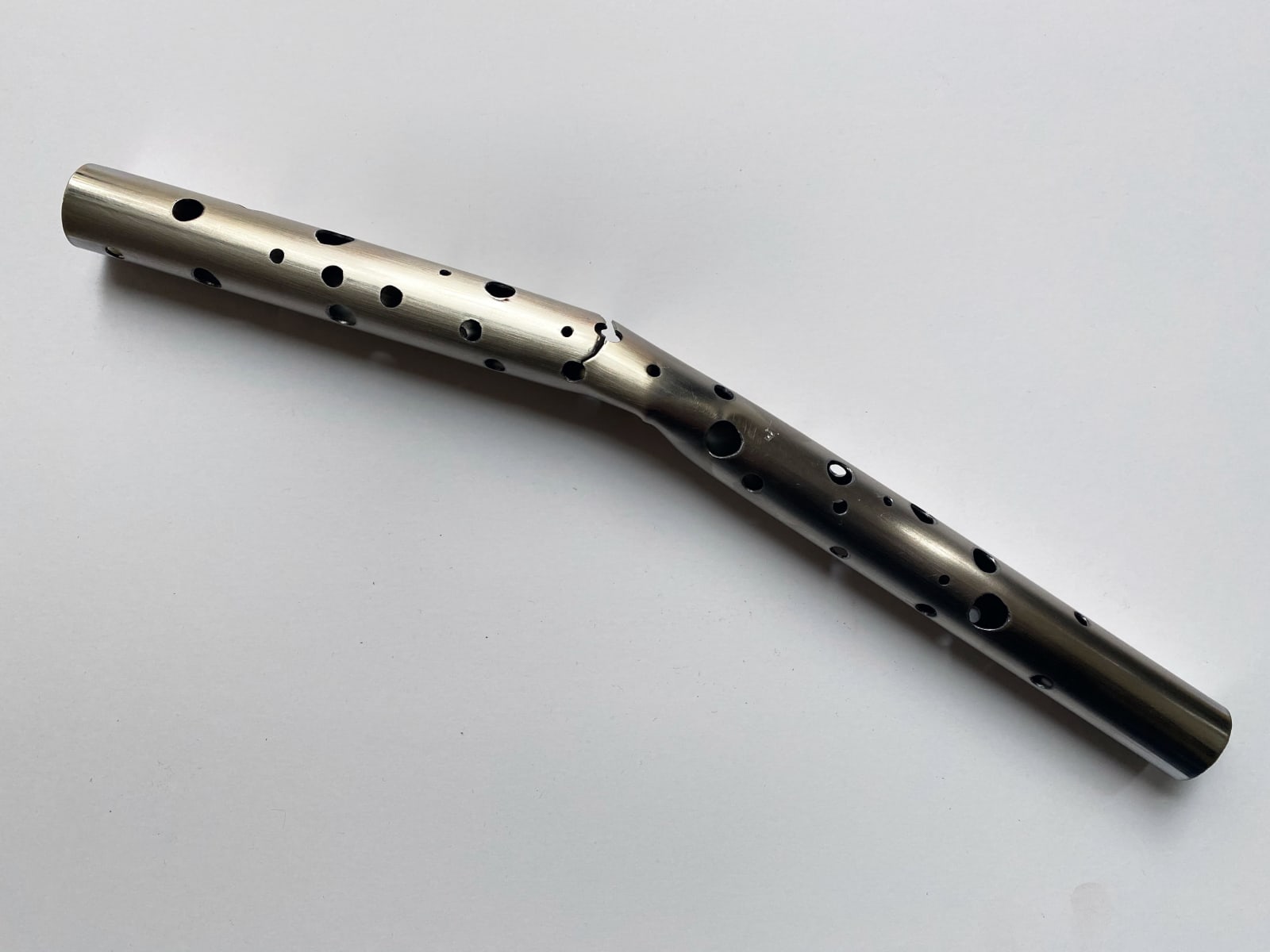 A metal rod that has been perforated with many small circular holes and slightly bent at the midpoint
