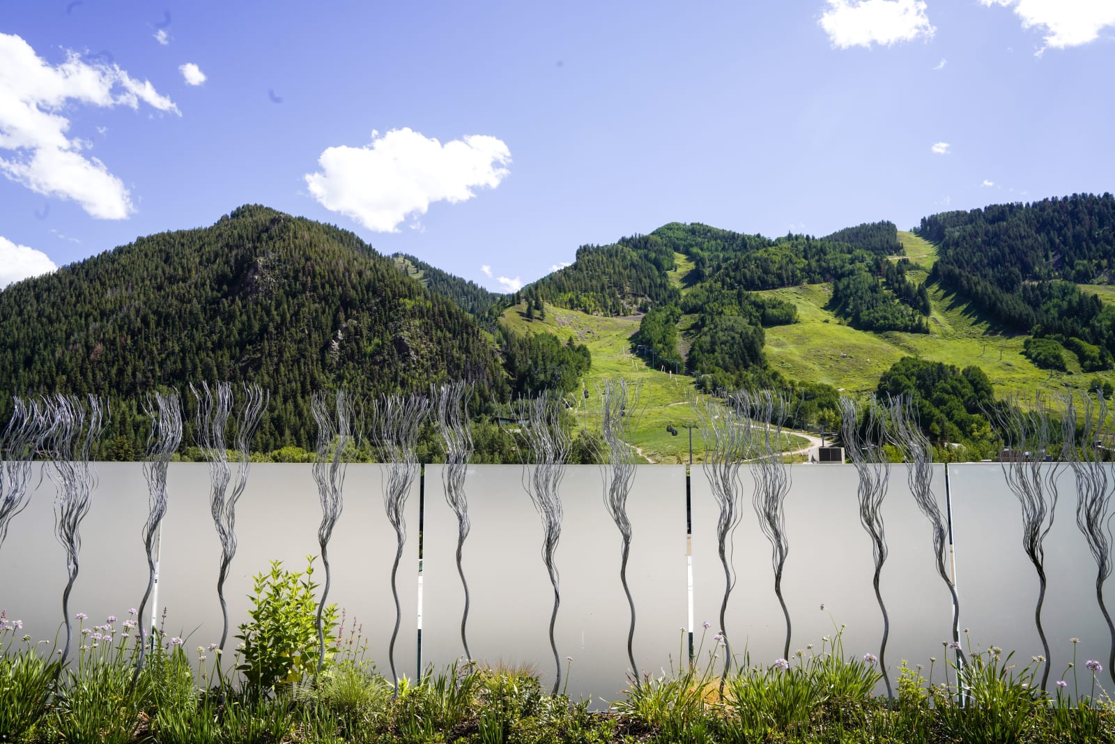Wire rope twisted to look like trees installed along a short wall in front of a hilly landscape