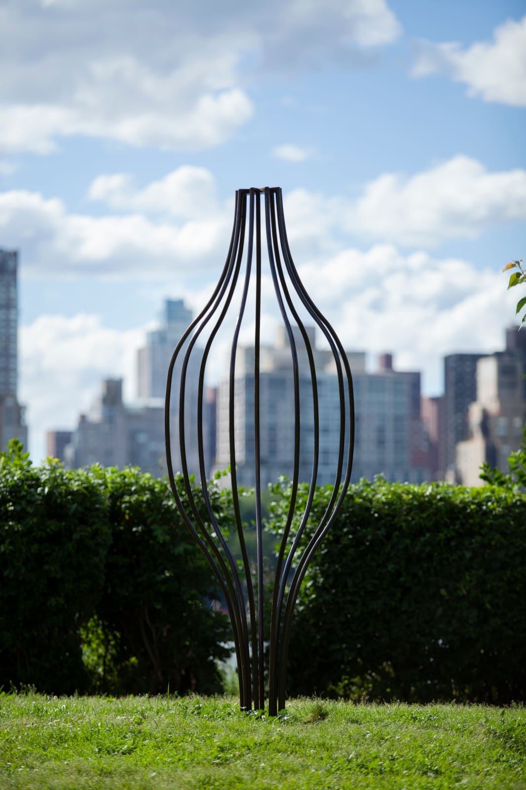 Outdoor installation view of a metal sculpture that resembles an unopened flower head at Socrates Sculpture Park