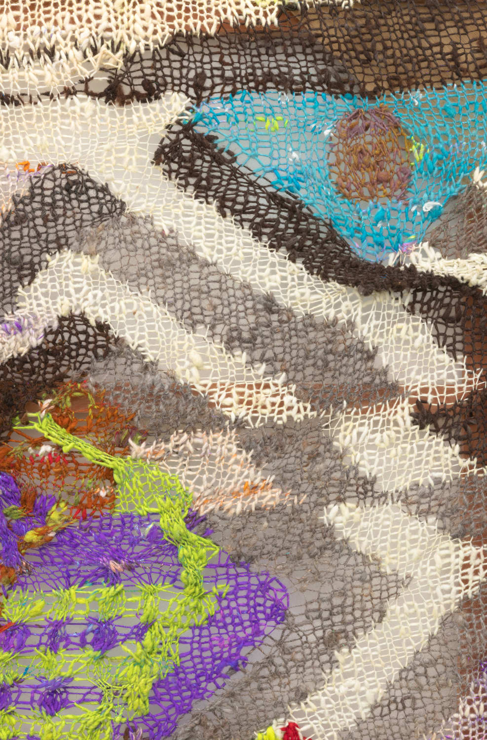 A close-up detail of geometric composition in multi-colored fibers stretched across a redwood frame as one would stretch a painting. The fibers are knit at varying thicknesses so that in places one can see through the stitches to the wall behind
