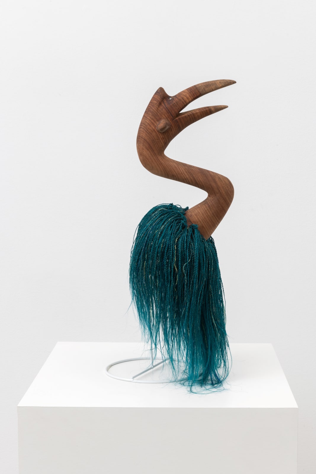 Sculpture made of blue synthetic hair and a wood bird head protruding from the top