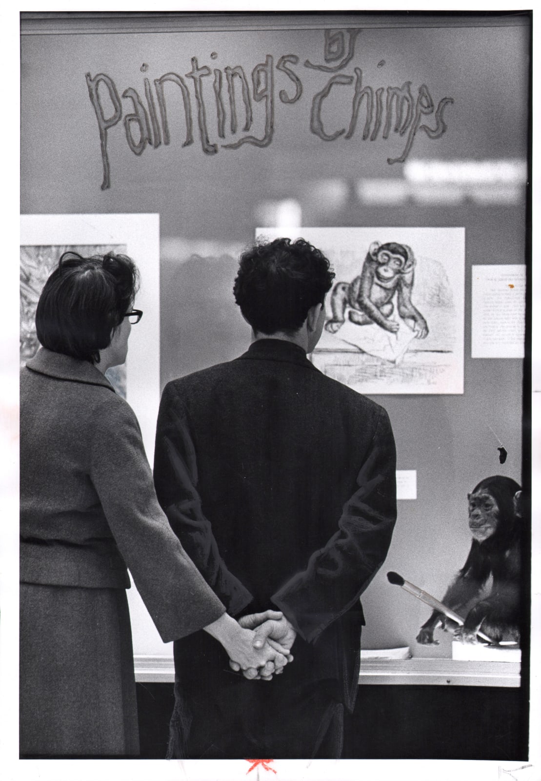 Black and white photograph of two people holding hands in front of Paintings by Chimps exhibition
