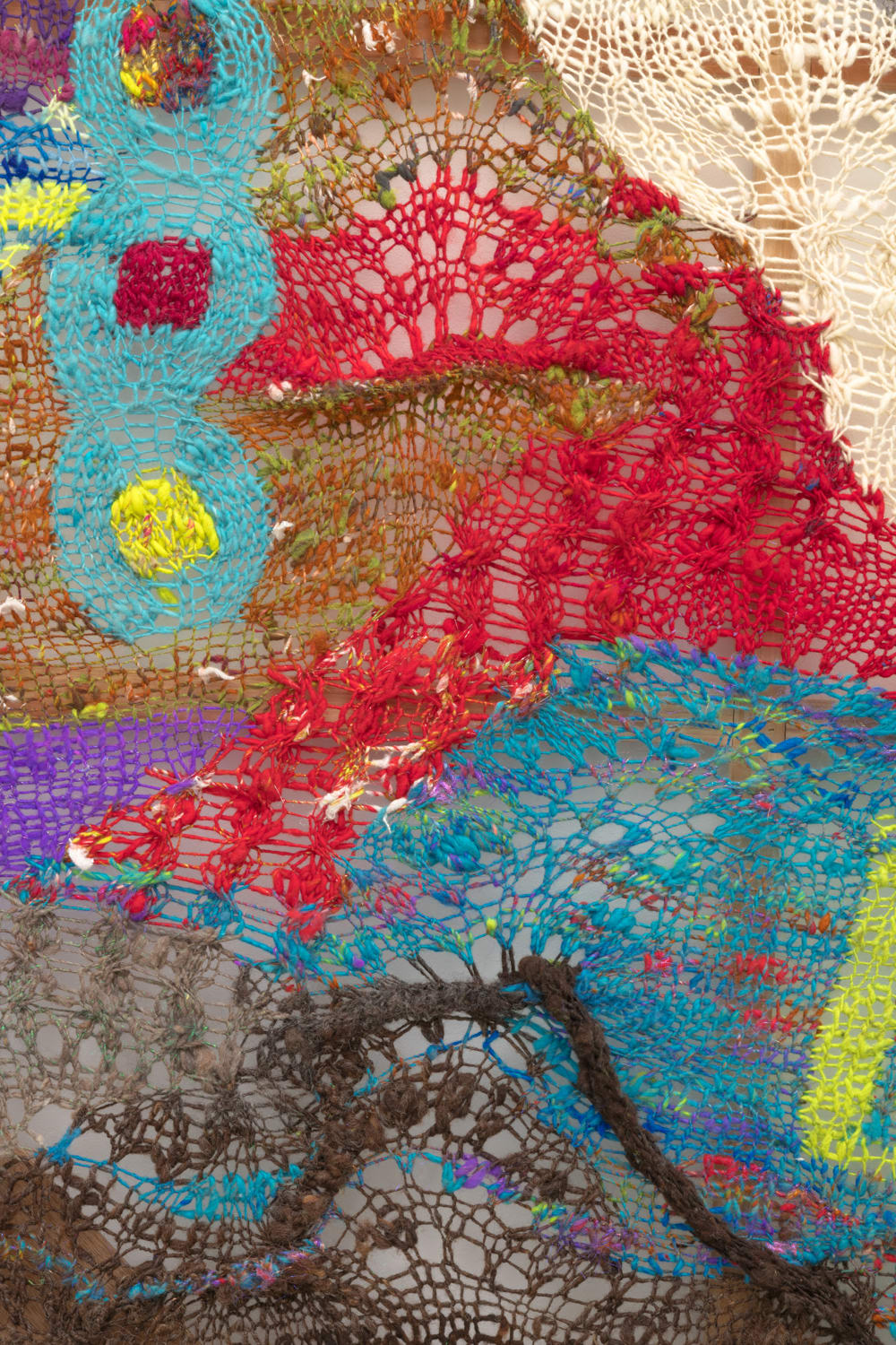 A detail shot of an organic composition with floating geometric accents in multi-colored fibers stretched across a redwood frame as one would stretch a painting. The fibers are knit at varying thicknesses so that in places one can see through the stitches to the wall behind.