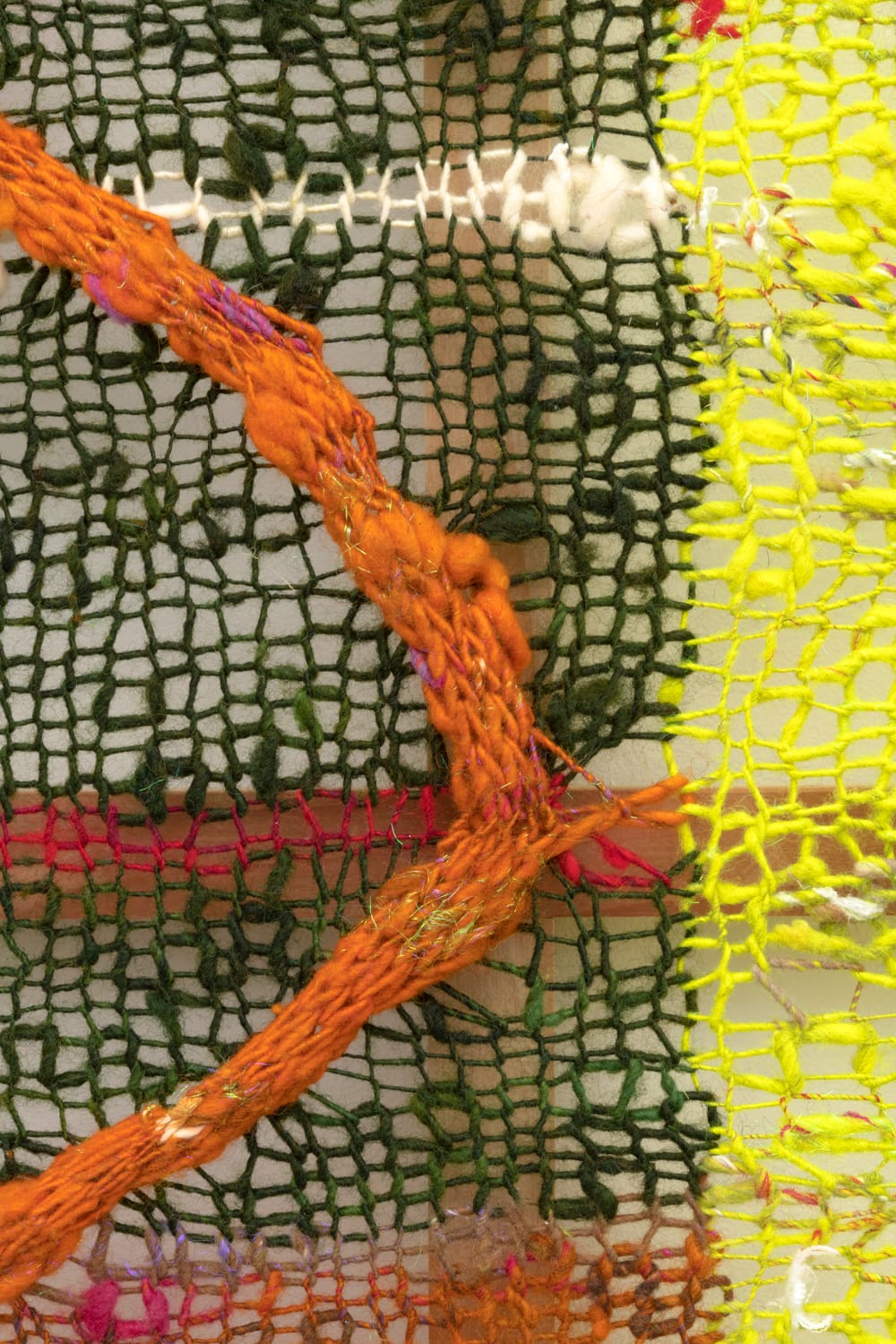 A detail of a striped but organic composition in multi-colored fibers stretched across a redwood frame as one would stretch a painting. The fibers are knit at varying thicknesses so that in places one can see through the stitches to the wall behind