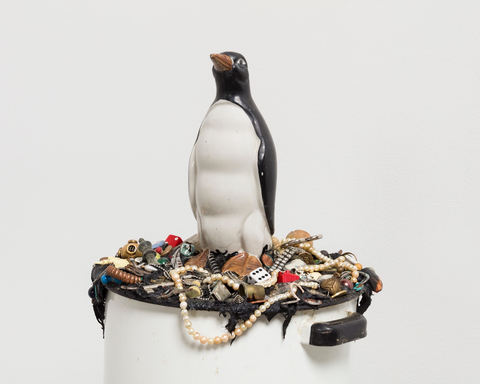 Cropped view of penguin sitting atop of a white pot filled with knick knacks