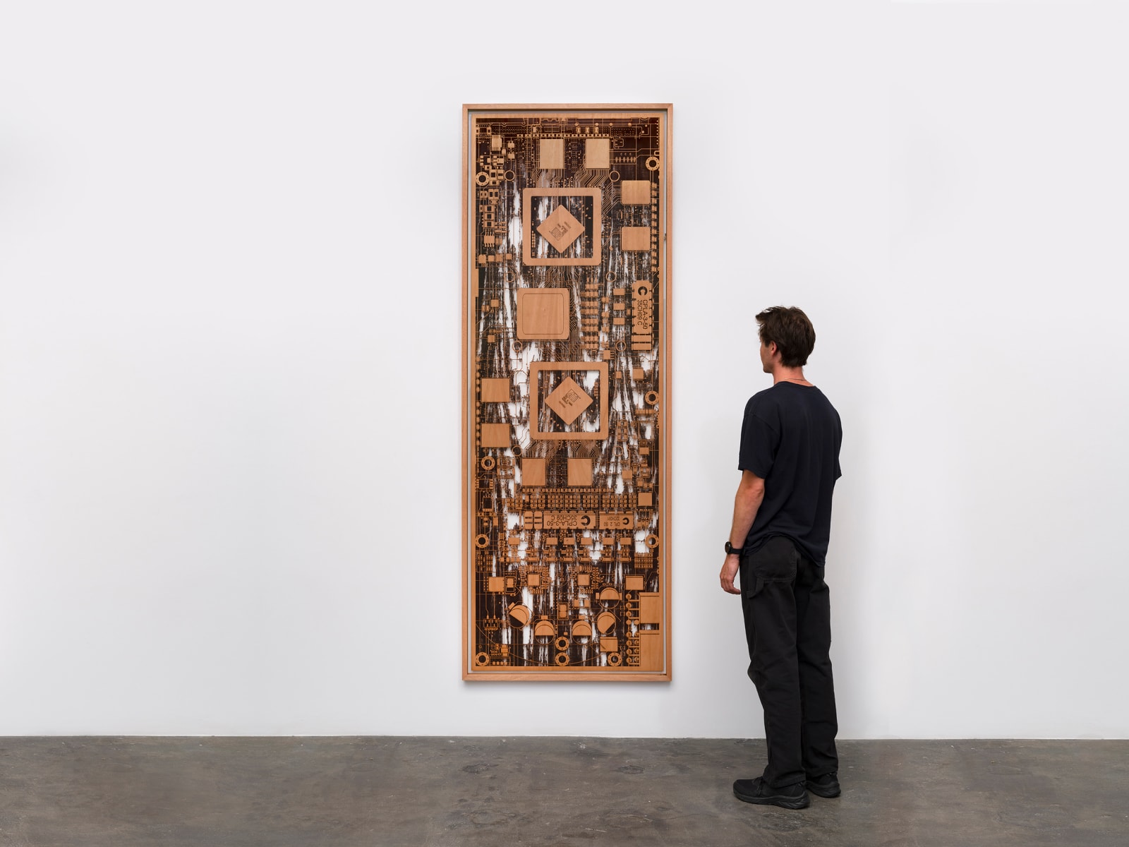 a wooden sculpture hung on a white wall with a figure looking at it