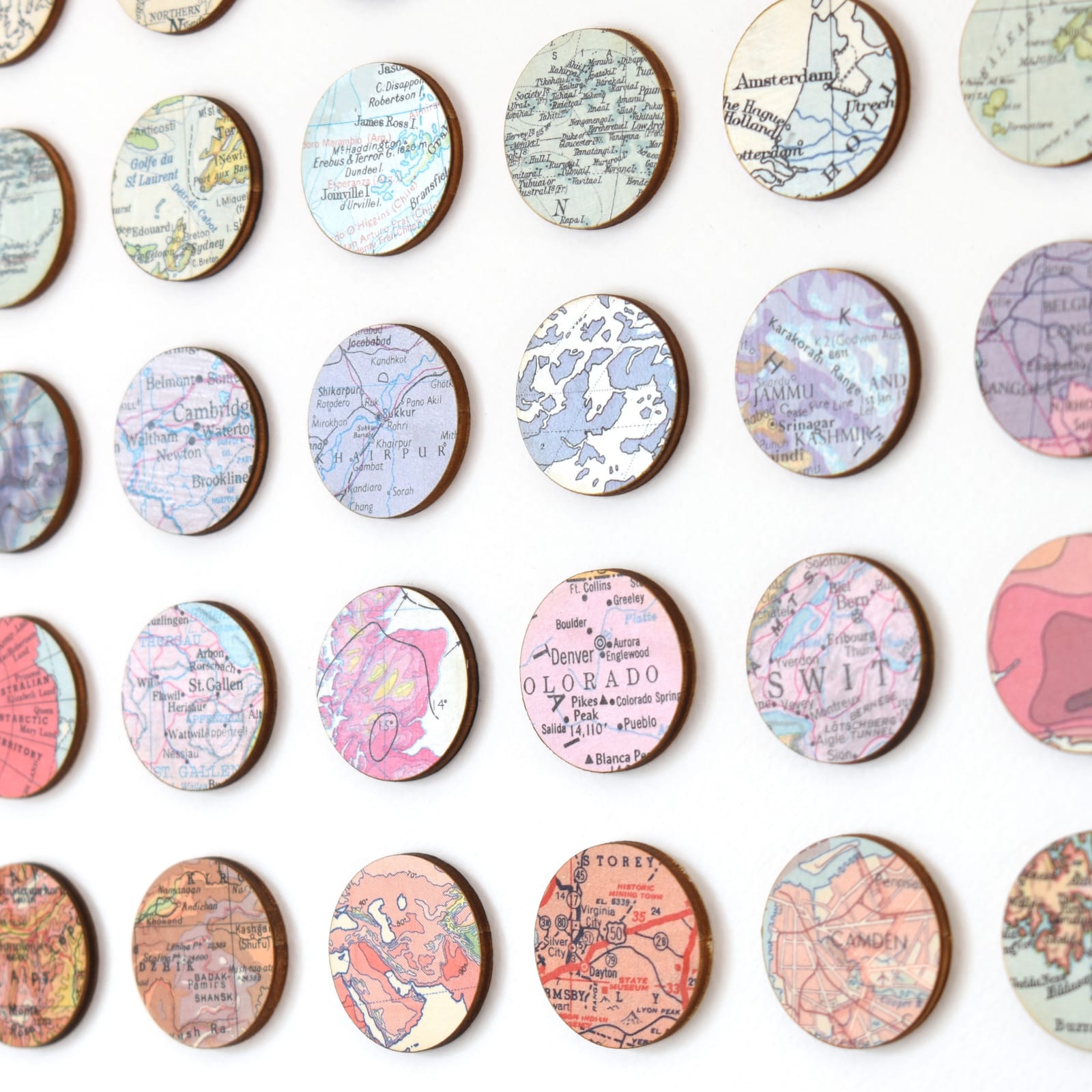 Close-up of a grid of circular cut-outs from vintage maps and atlases, each mounted on birch wood and arranged by colour gradient on a white background.