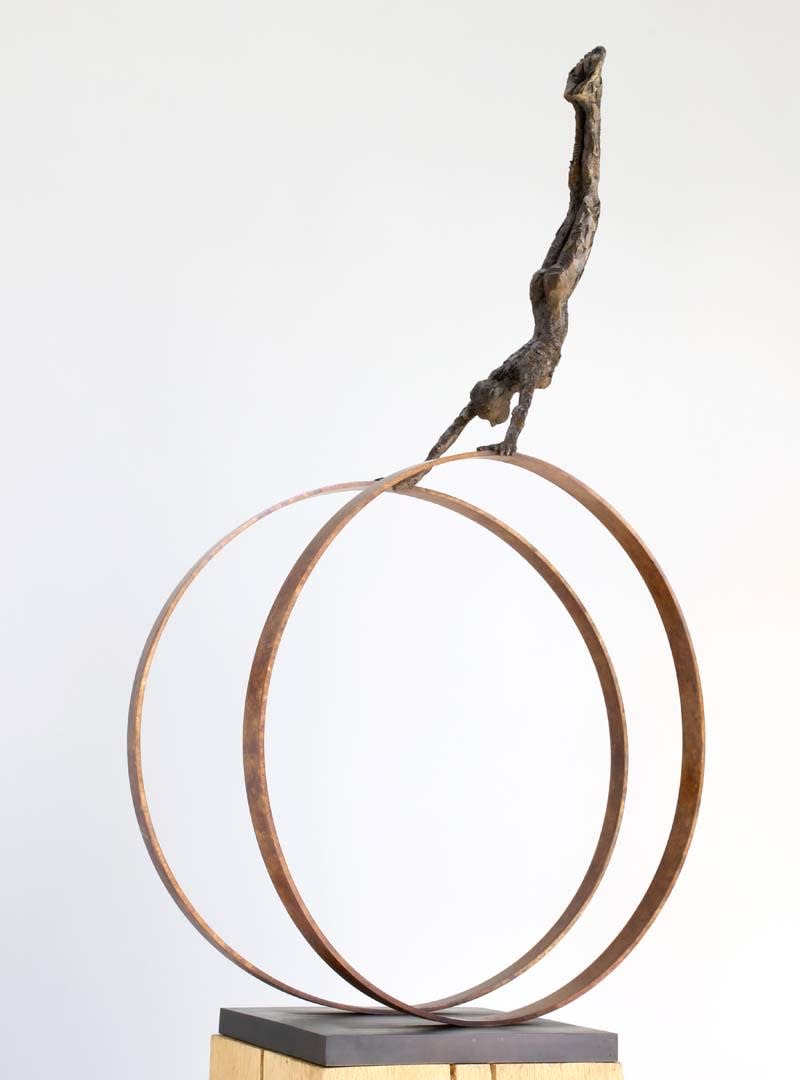 Two large bronze rings with sculpture doing a handstand on top