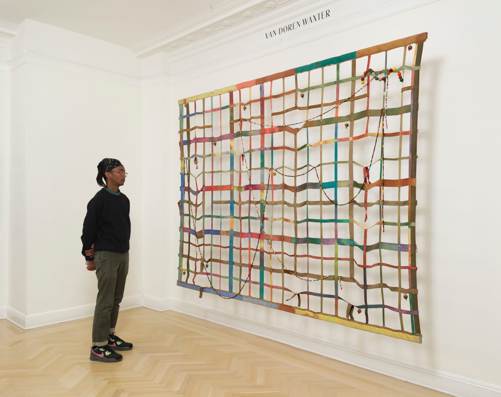a large gridded painting hanging off the wall with a man standing next to it for scale