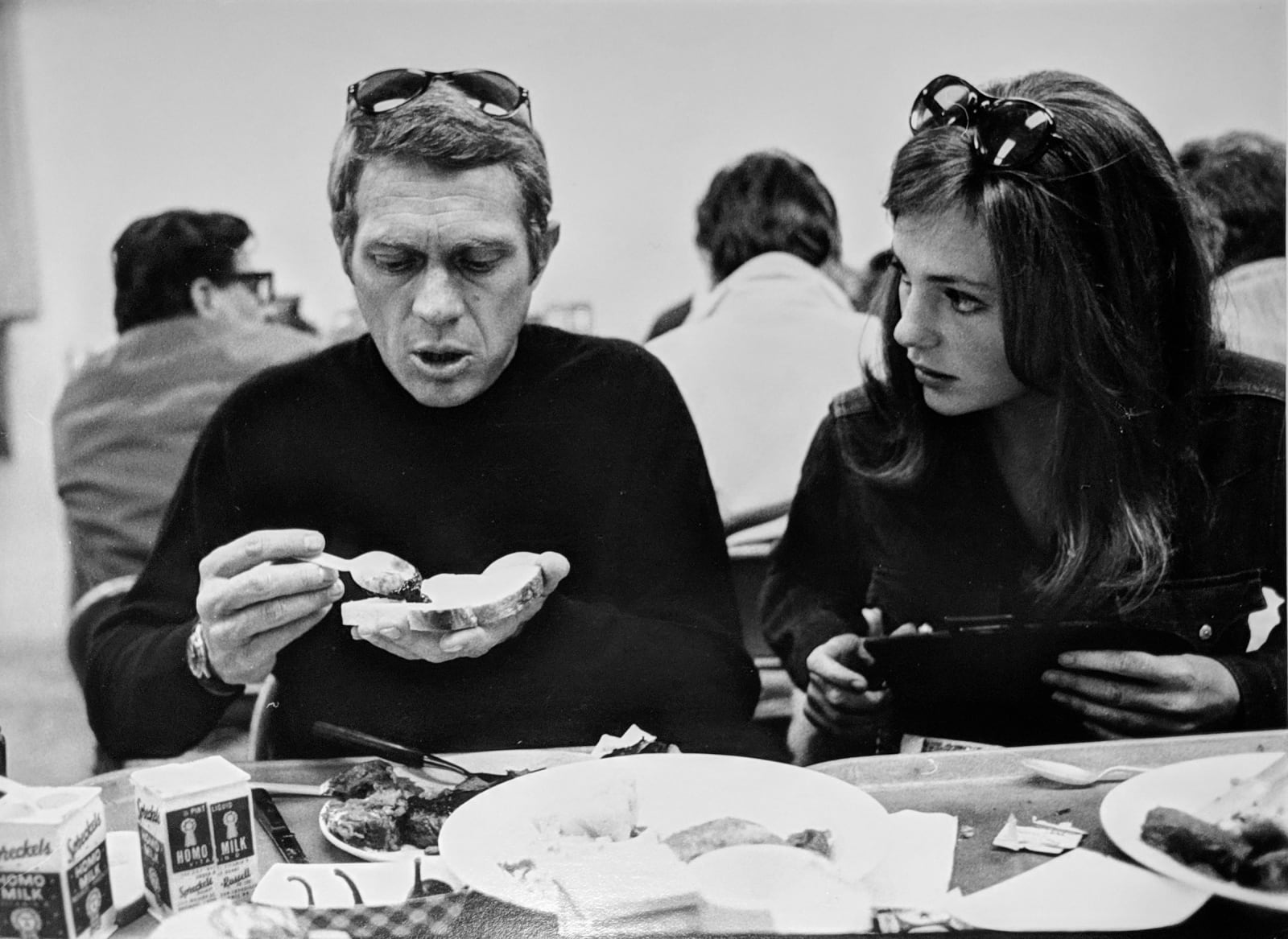 Black and white photograph of Steve McQueen and Jacqueline Bissett sitting down and speaking while Mcqueen makes a sandwich at lunch , on the set of “Bullitt”