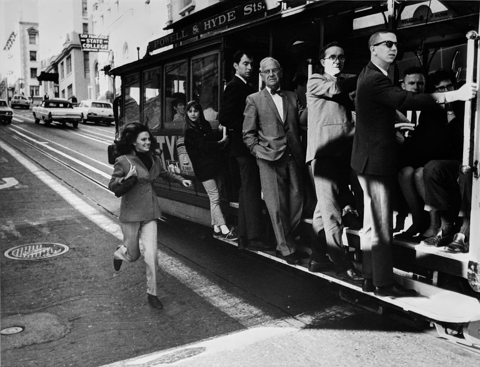 Black and white photograph of Jacqueline Bissett running alongside a packed tram on the street, on the set of “Bullitt”