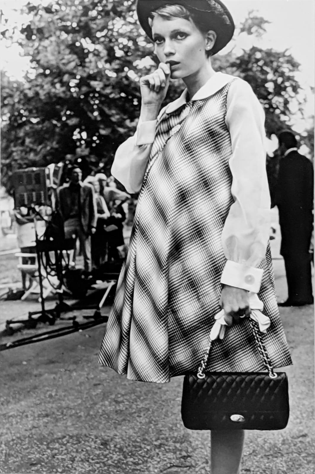 Black and white photograph of Mia Farrow in Central Park, wearing a plaid dress on the set of “Rosemary's Baby”