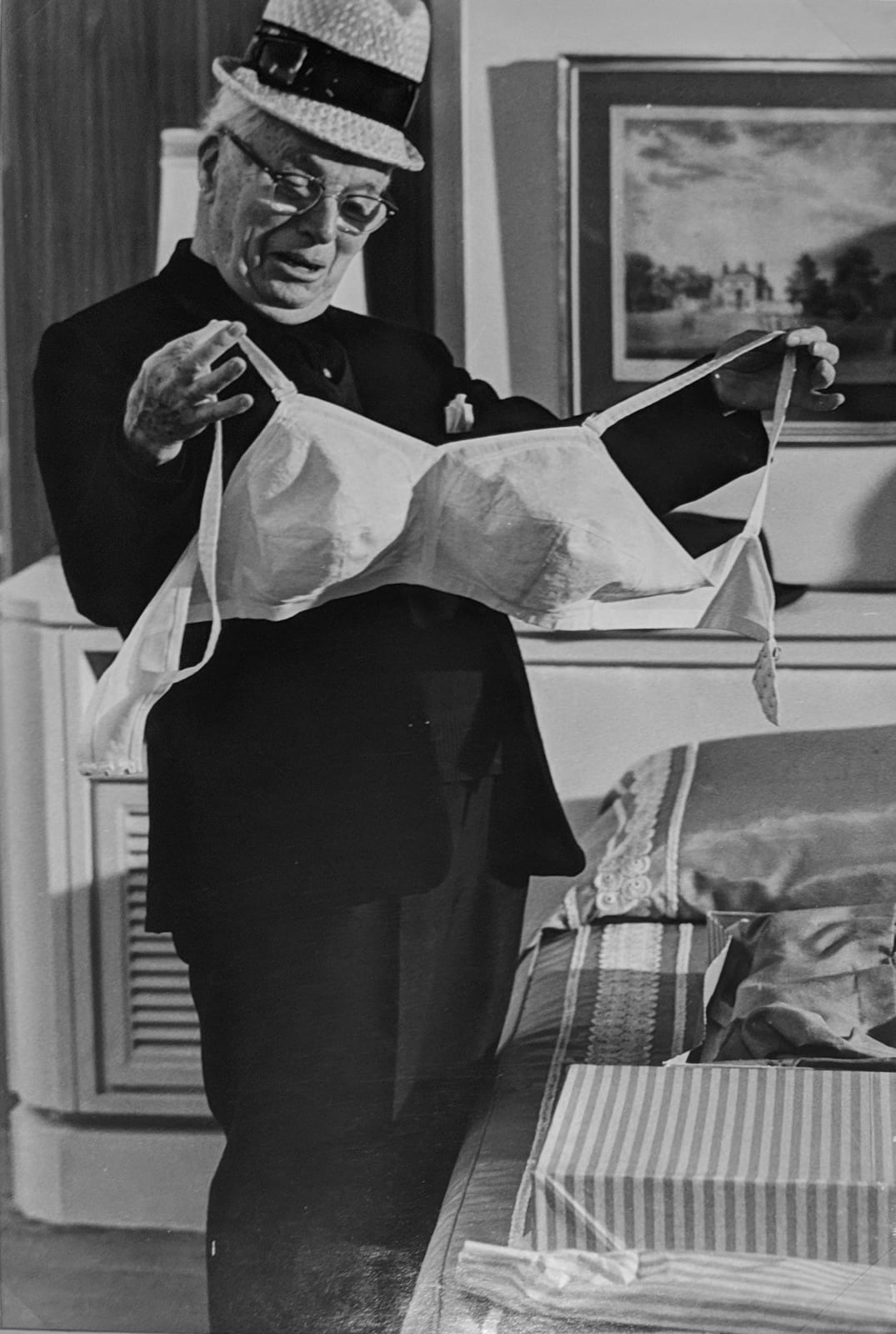 Black and white photograph of Charlie Chaplin holding a large white bullet bra on the set of “A Countess from Hong Kong”