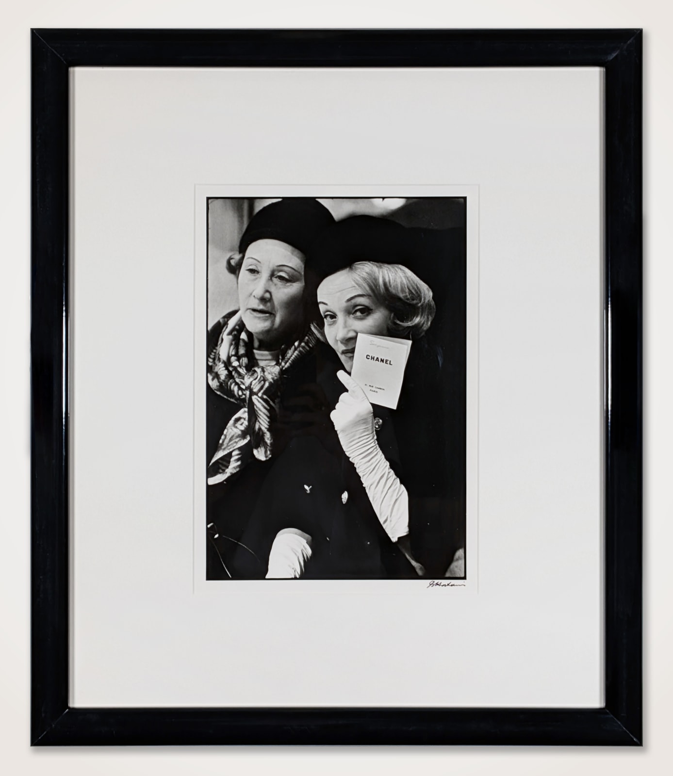 Framed black and white photograph of Marlene Dietrich sitting next to a patron holding a Chanel card at a fashion presentation at the House of Chanel