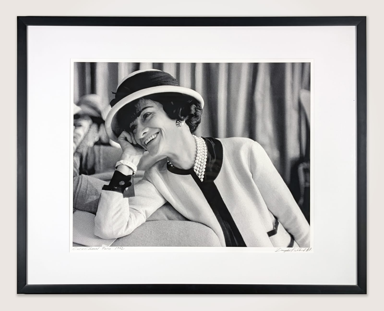 Framed black and white photograph of Designer Coco Chanel laughing on the couch