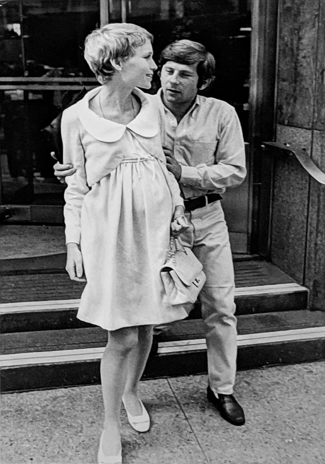 Black and white photograph of Roman Polanski holding Mia Farrow from behind in front of The Dakota Building, New York City, on the set of “Rosemary's Baby”