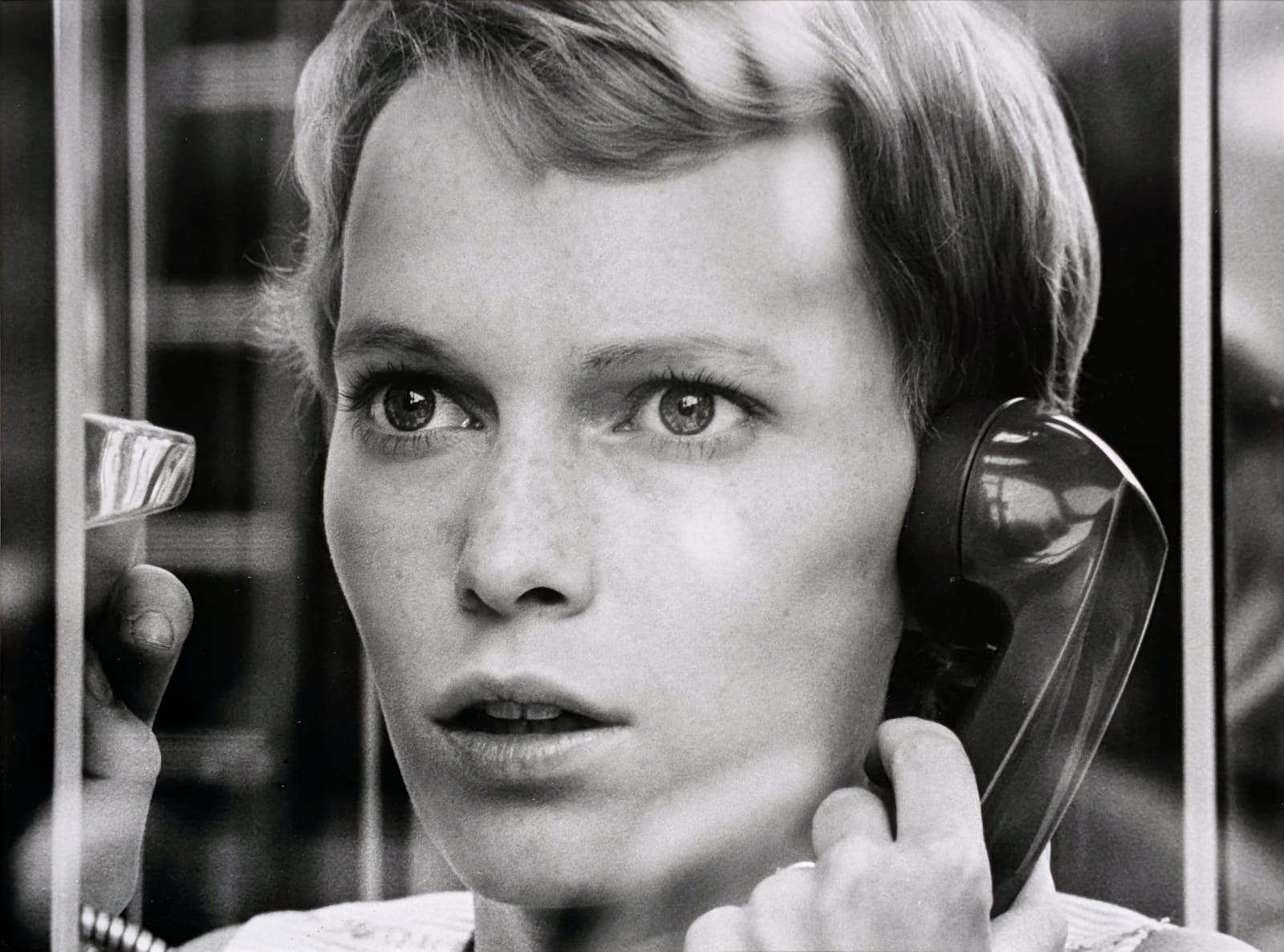Black and white photograph of Mia Farrow looking out the window on the phone, with a tense look on her face, on the set of “Rosemary's Baby”