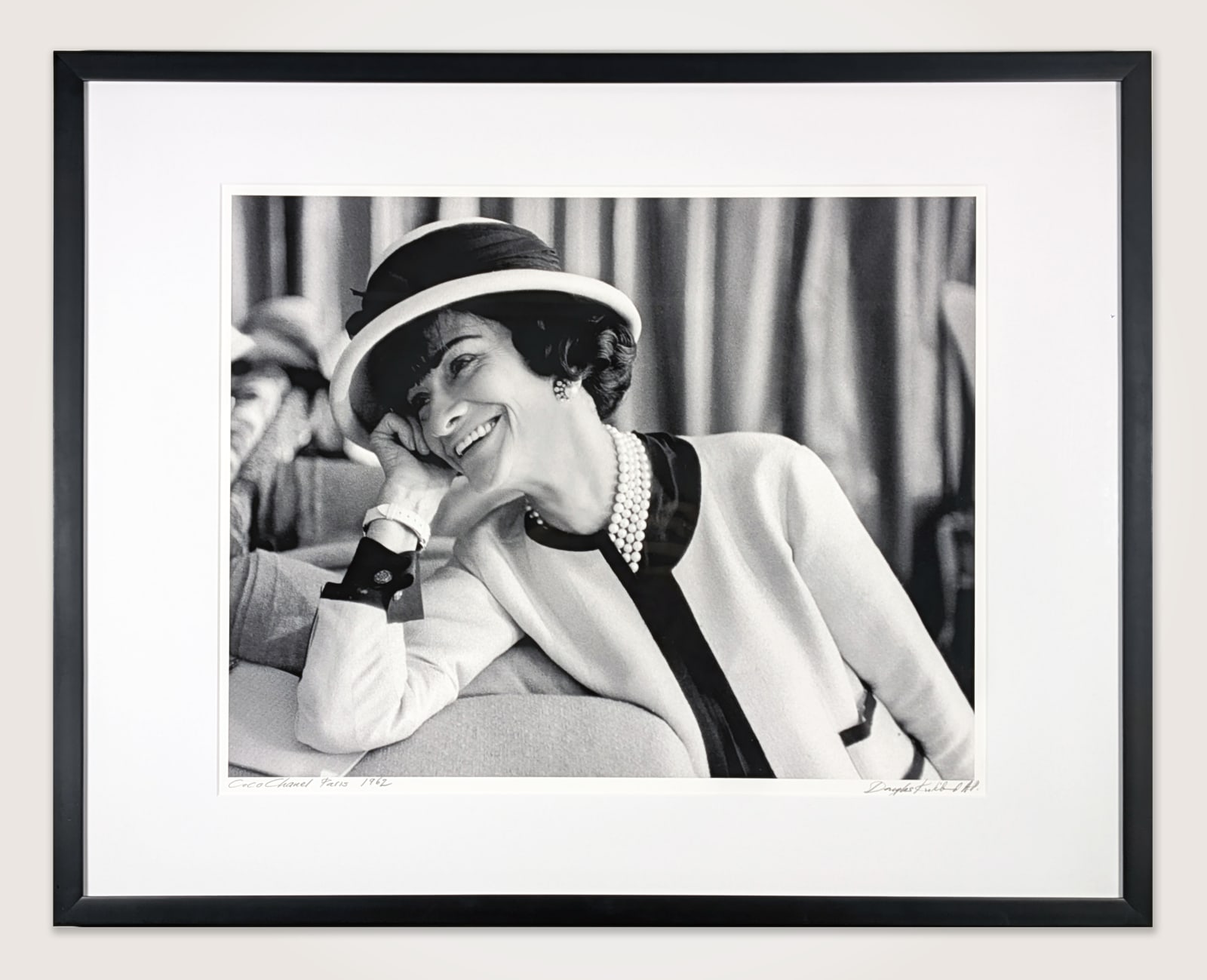 Framed black and white photograph of Designer Coco Chanel laughing on the couch