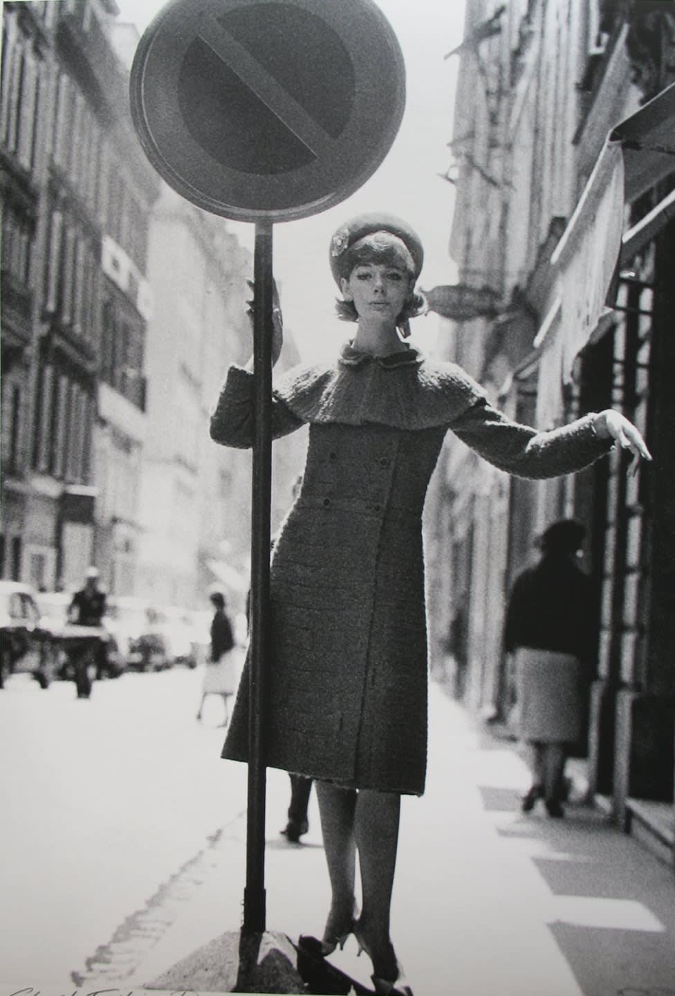 Black and white photograph of a model presenting a Chanel outfit balancing on a stop sign in the streets of Paris