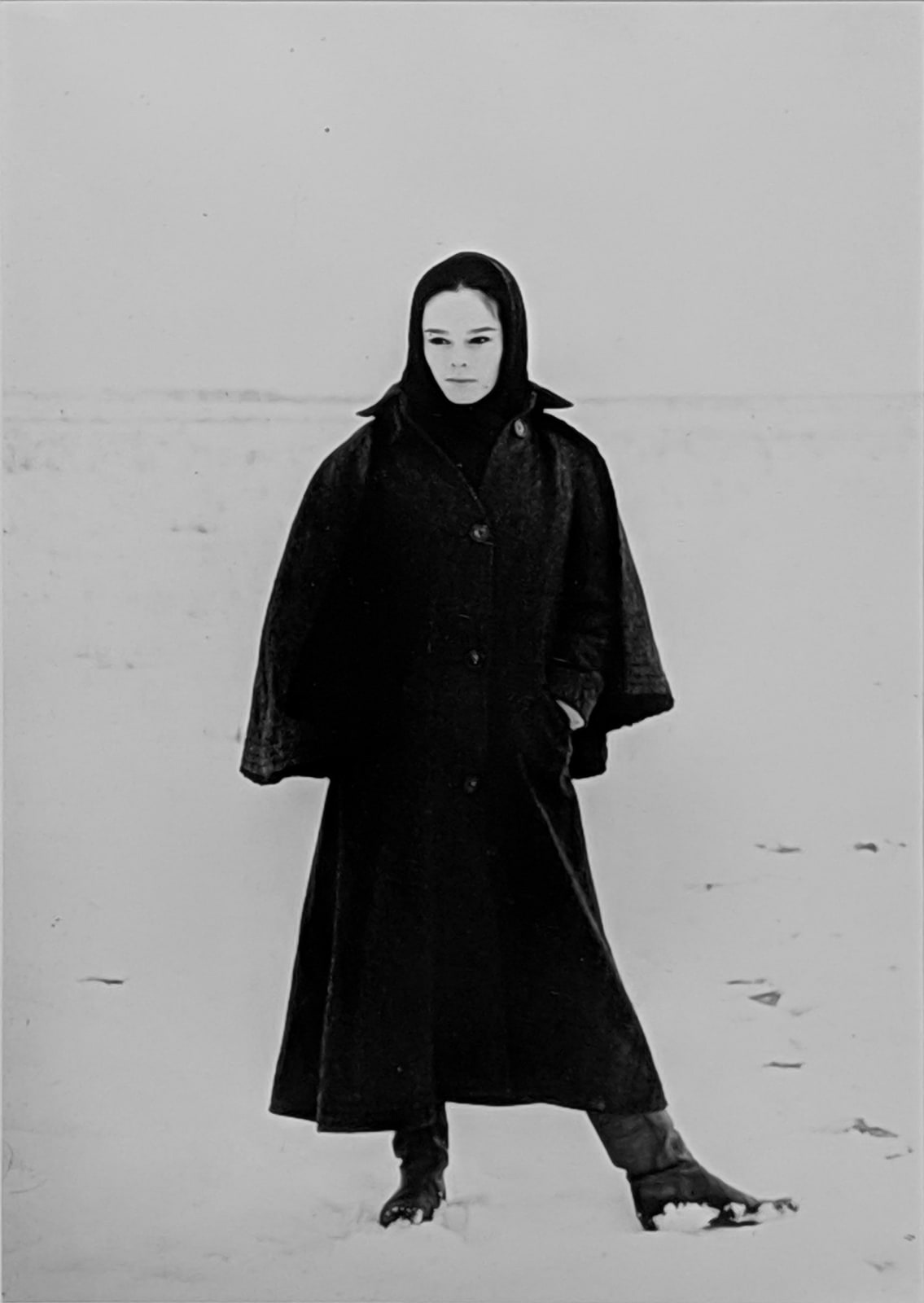 Black and white photograph of Geraldine Chaplin posing towards the camera wearing an all black winter outfit, preparing for a scene in the harsh tundra