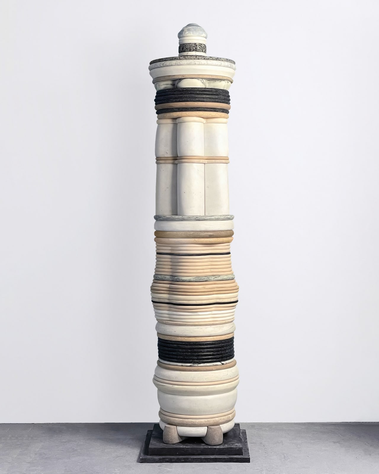 Human-scale totemic sculpture comprising varied layers of carved marble and stone