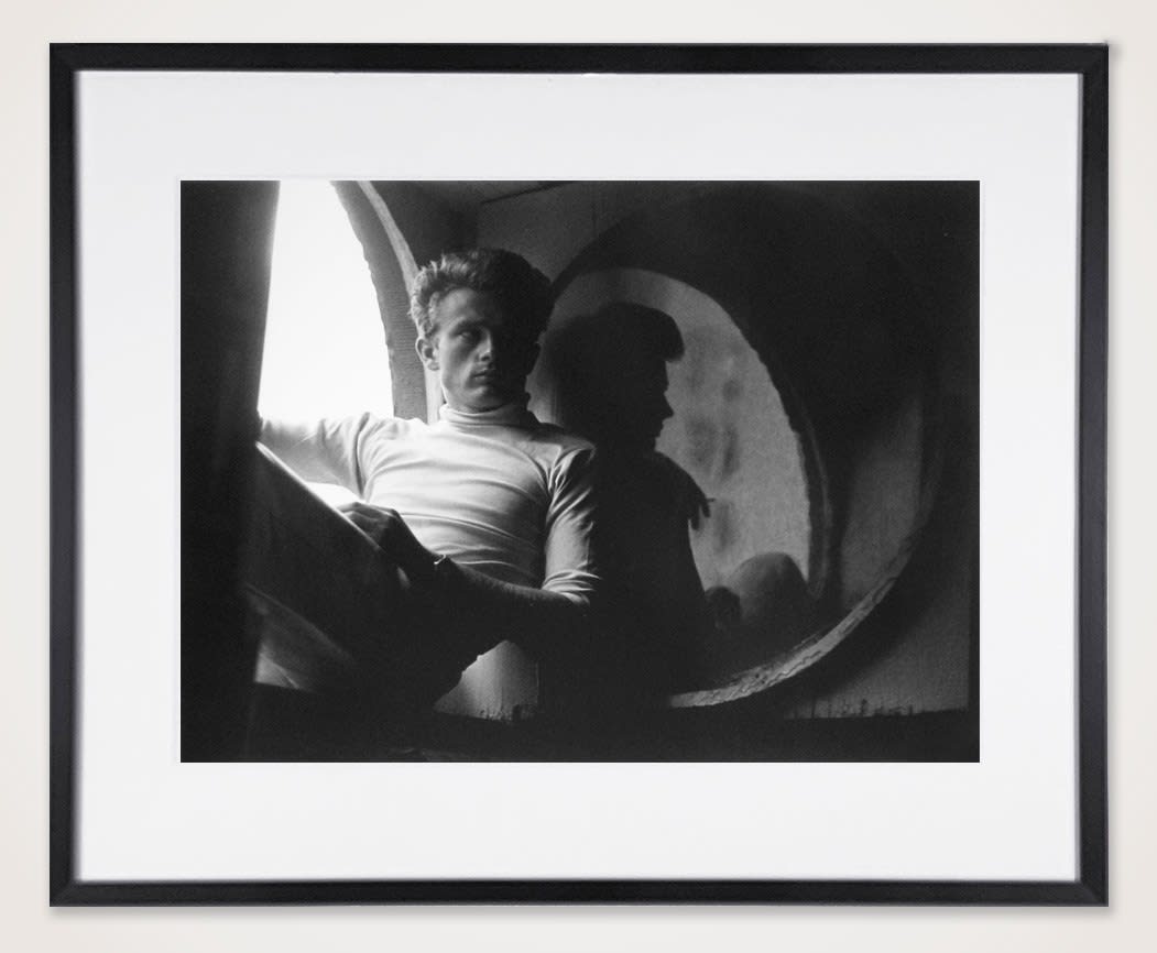 Framed bBlack and white photograph of James Dean sitting by a window holding a book in an apartment setting