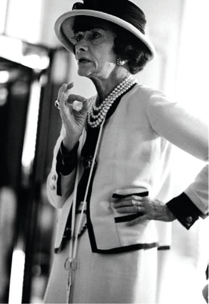 Black and white photograph of Designer Coco Chanel gesturing with her hand on her hip